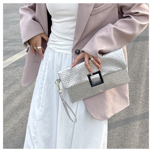 Detail of silver envelope clutch bag with textured finish and black buckle on handle