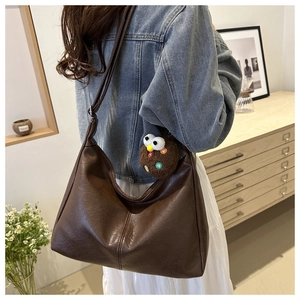Detail of a large brown faux leather hobo bag with litchi texture and a plush charm