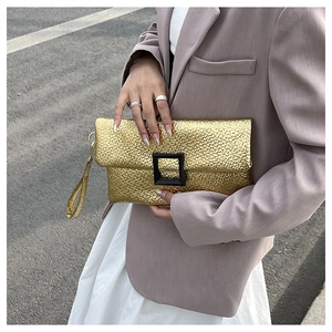 Close-up of a gold pleated clutch with a large black square buckle and wrist strap