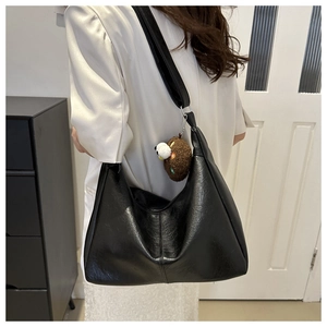 Detail of black lychee texture PU hobo bag with wide strap and plush bear charm