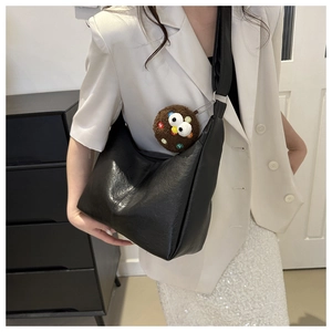 Detail of black faux leather hobo bag with a plush brown eye charm on white suit
