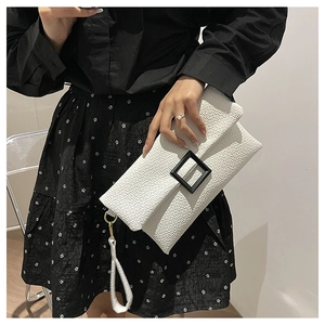 Close-up of white textured envelope clutch featuring a bold black square buckle and wristlet