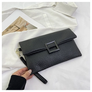 Detail of textured black envelope clutch bag with matte square buckle and wristlet strap