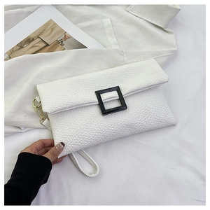 Detail of white textured envelope bag featuring a black square buckle and gold hardware