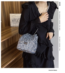 Close-up of silver sequin bucket bag with metal chain strap on model in black dress