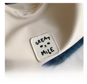 Détail du sac bandoulière en nylon beige avec logo Great Mile et broderie de dessin animé