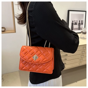 Detailed view of an orange quilted chain bag worn by a model in a stylish indoor setting