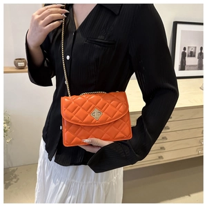 Detail of orange quilted crossbody bag featuring a golden X-shaped metallic twist lock