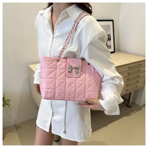 Detailed view of pink quilted shoulder bag with metal bow accent and chain strap worn by model