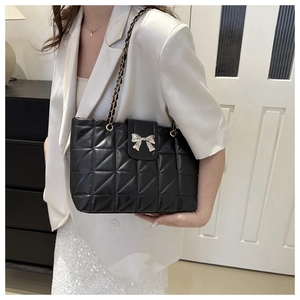 Close-up of black quilted shoulder bag featuring a silver metal bow and chain strap