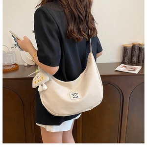 Détail du sac demi-lune en nylon beige avec logo et pendentif smiley en peluche
