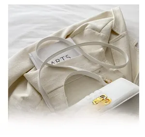 Détail d'un sac bandoulière blanc matelassé avec boucle BB dorée sur un blazer beige
