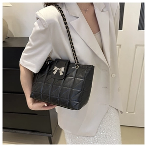 Detail of black quilted tote bag featuring silver bow ornament and chain strap