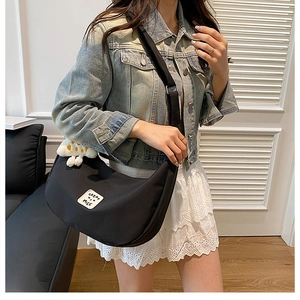 Détail du sac bandoulière demi-lune en nylon noir avec breloque nuage et étiquette tissée