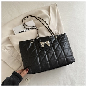Detail of black quilted shoulder bag featuring a silver metal bow and chain strap