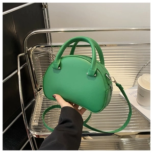 Detail of sage green pod-shaped handbag featuring round handles and detachable strap