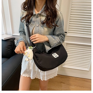 Détail d'un sac bandoulière demi-lune en nylon noir avec logo souriant et bijou nuage