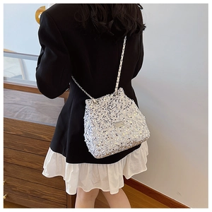 Detail of silver sequin bucket bag featuring a sleek metal logo and fine chain strap