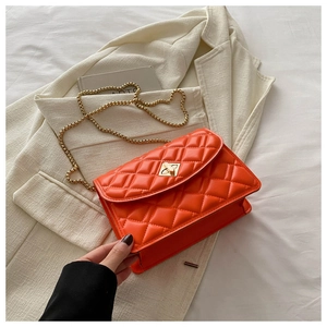 Detail of orange quilted crossbody bag featuring a gold chain strap and metal twist lock