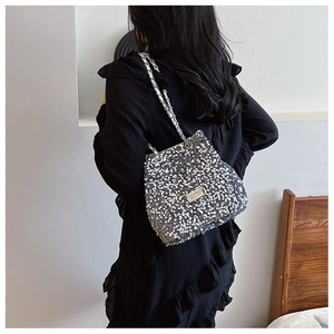 Detail of silver sequined bucket bag with metallic chain strap shown on a black dress
