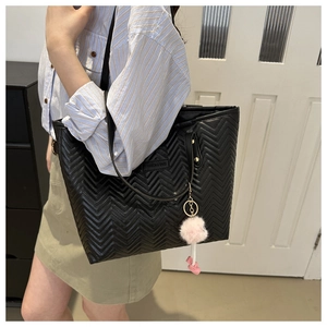 Close-up of black quilted bucket bag with wave stitching and pink pompom keychain detail