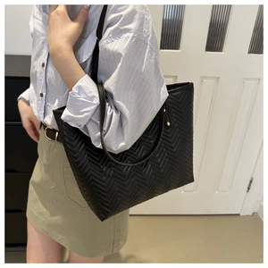 Detail of black quilted tote bag with V-shaped stitching and slender shoulder strap