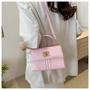 Sac à bandoulière en cuir mat rose avec boucle dorée porté par un mannequin
