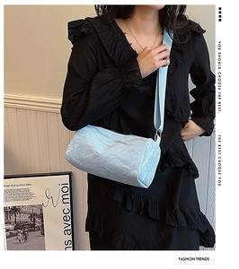 Detail of light blue cylindrical crossbody bag featuring unique pleated texture and wide strap