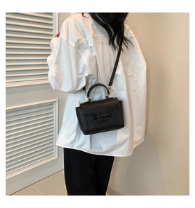 Detail of black lychee grain crossbody bag with gold hardware on white shirt model