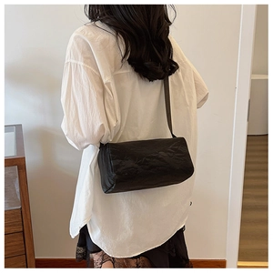 Minimalist black cylinder crossbody bag with crinkle texture shown on a model