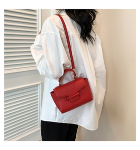 Back view of model carrying a red litchi texture small square bag with metal bar detail