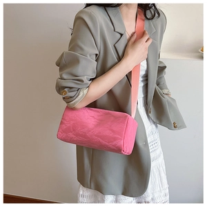 Pink cylinder pillow bag with pleated texture and wide woven strap on a model