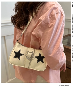 Close-up of beige shoulder bag featuring black star patches and silver star hardware