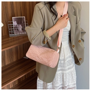 Pink cylinder pillow bag with pleated texture and wide strap worn by a model