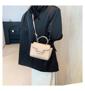 Crossbody shot of a cream leather small square bag with flap closure and adjustable strap