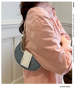 Model wearing a charcoal denim half-moon underarm bag with beige leather trim and gold buckle