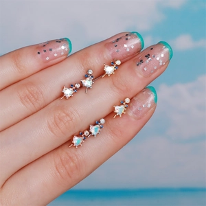 Luxuriöse Herz-Ohrstecker mit Opal und Kristallen vor einem blauen Himmelshintergrund