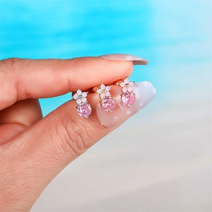 Three-piece set of pink flower stud earrings with gold finish, held between fingers