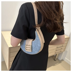 Blue denim crescent underarm bag with beige leather trim and gold buckle worn by model