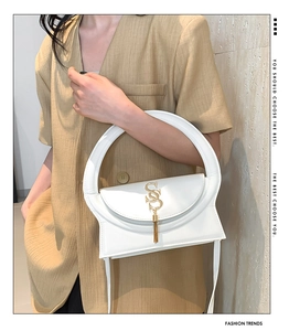 Detail of white leather shoulder bag with circular handle, gold S logo and tassel