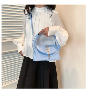 Detail of light blue crossbody bag with large round handle and golden fringe logo
