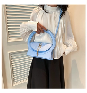 Detail of light blue shoulder bag featuring large round handle and gold tassel charm