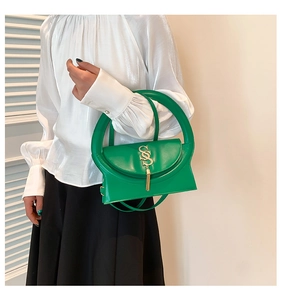 Detail of green handbag with oversized round handle and golden S-shaped buckle