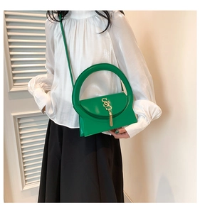 Detail of bright green handbag featuring a round handle and gold tassel logo pendant