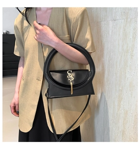 Detail of black leather handbag featuring round cutout handle and gold tassel logo
