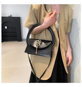 Detail of black leather handbag with round handle and gold SS fringe on beige blazer