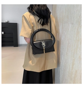 Detail of black leather handbag with unique gold hardware and tassel on beige blazer