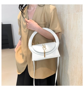 Close-up of white minimalist shoulder bag featuring golden S logo and tassel detail