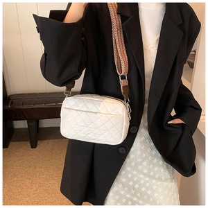 Weiße Stepptasche mit geometrischem Schultergurt getragen von Model im schwarzen Blazer