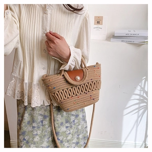 Detail of hand-woven basket bag featuring a brown leather flap and a white pearl buckle